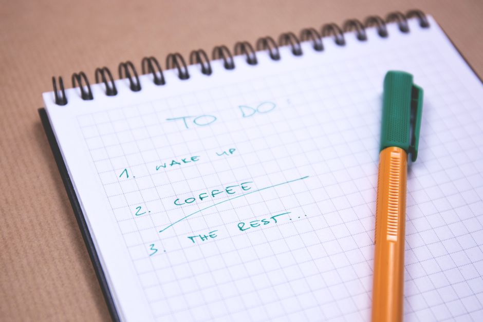 A handwritten checklist on graph paper beside an orange and green pen.